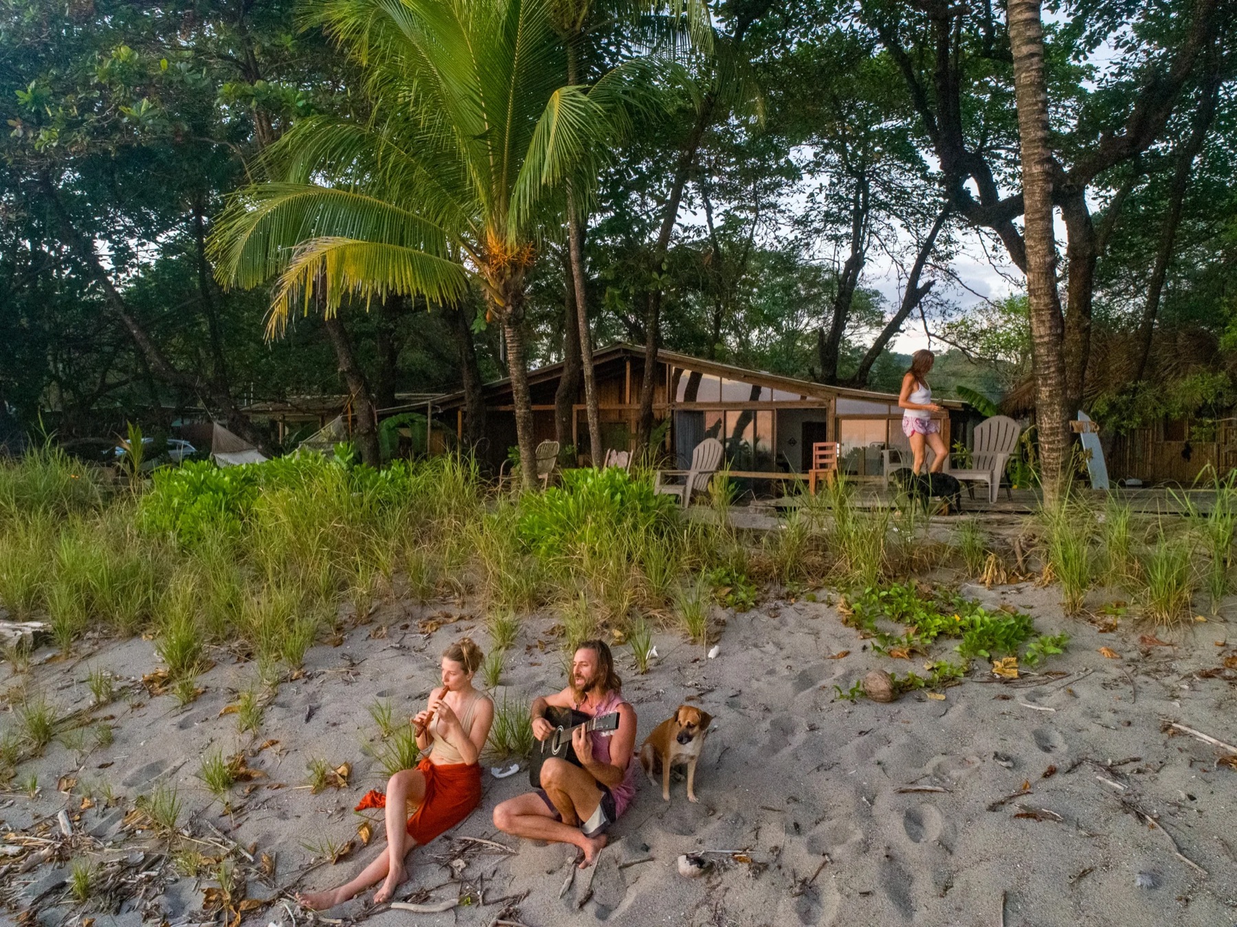 Guitar and flute on the sand in front of House of Waves at golden hour, with a dog listening